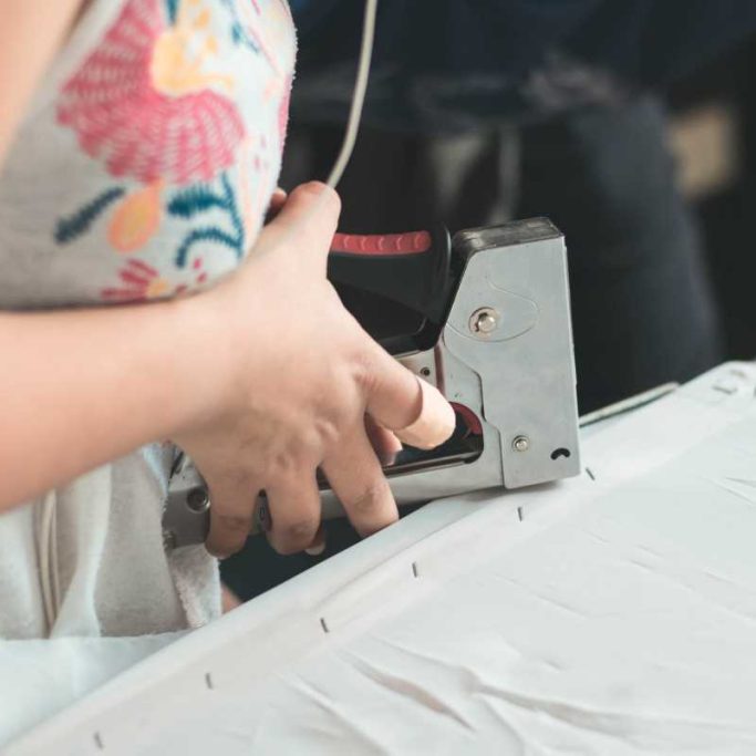 A lady using a staple gun to secure fabric to a frame in a craft project