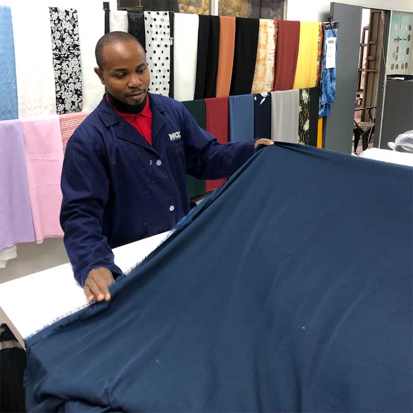 An employee, in front of a fabric display, measuring and folding fabric on a table